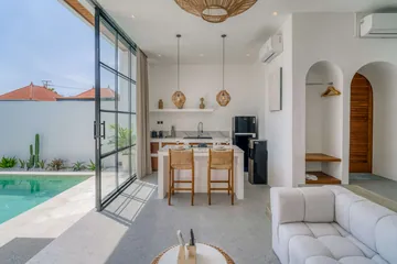 Dining island and kitchen beside glass doors to the pool, with an arched timber door and sofa.