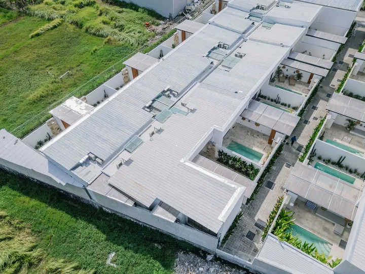 Aerial view of a row of low-rise buildings among green plots and surrounding rooftops.