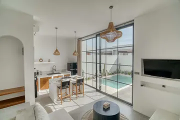 Kitchen island with dark chairs beside full-height glass doors, with a wall-mounted television.