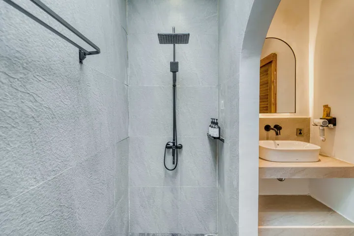 Walk-in shower with dark shower fittings beside a narrow vanity and arched mirror.