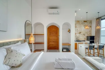 Bed in the foreground with an arched timber door and kitchen dining area beyond.