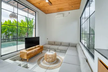 Living room with a white sectional, low timber table and television beside tall glazing.