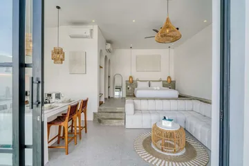 Bright bedroom and lounge with white bed and sectional beneath woven pendants.