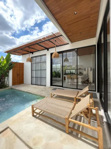 Timber loungers along the pool edge, below a slatted roof and a bright sky.