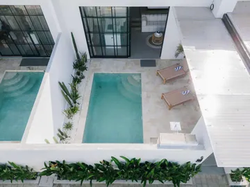 Aerial view of two neighbouring courtyard pools separated by a planted white wall, with loungers.