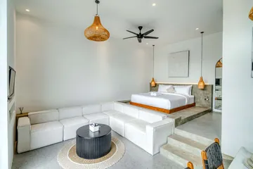 Pale sectional sofa and low bed in a bright room with a round coffee table.