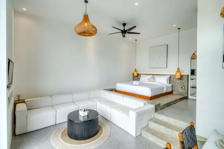 Pale sectional sofa and low bed in a bright room with a round coffee table.