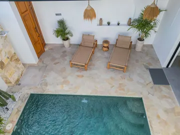 Overhead view of a rectangular pool beside pale paving and two wooden loungers.