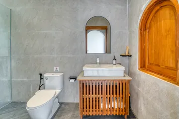 Bathroom vanity and toilet framed by an arched wood opening.