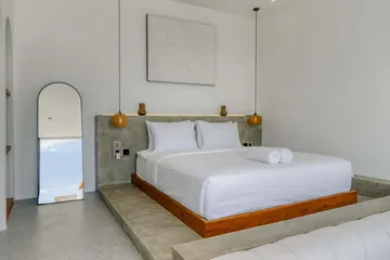 White bed with wood frame against a textured pale wall.