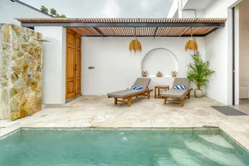 Courtyard pool and stone deck facing a white arched wall and timber pergola.