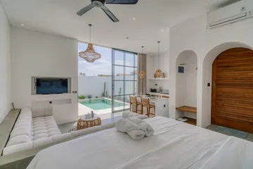 White bed with wood base against pale wall, with arched mirror and bedside shelf.