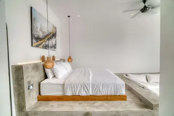 Low bed on a timber platform against a stone headboard wall, beside a sectional sofa.