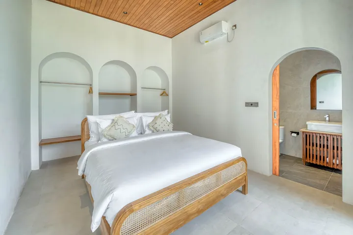 A bedroom with white linen, a timber ceiling and an arched doorway to the bathroom.