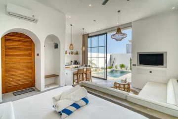 Wide bedroom view combining a white bed, built-in seating, television and dining counter.