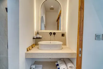 An arched bathroom mirror, pale stone basin and timber detailing.