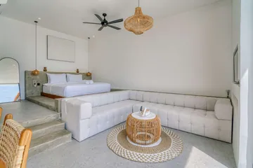 Open bedroom and lounge with white bed, sectional and ceiling fan.