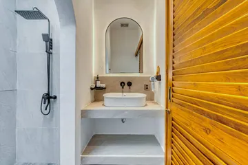 An arched bathroom mirror, pale stone basin and timber detailing.