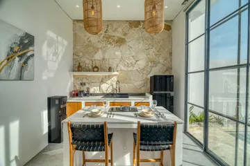 Dining table and stone-backed kitchen with dark chairs, viewed through the open living space.