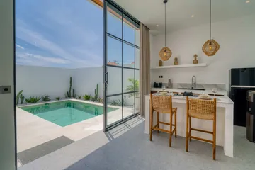 Kitchen counter with woven stools beside full-height glass doors open to the courtyard pool.