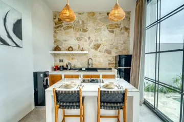 Dining table and kitchen island against a stone wall, beside full-height glazing.
