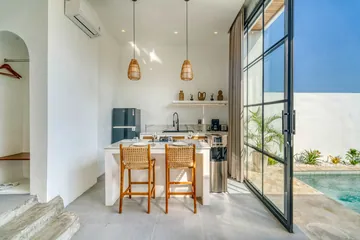 Dining table and kitchen island beside glass doors, with planting visible outdoors.