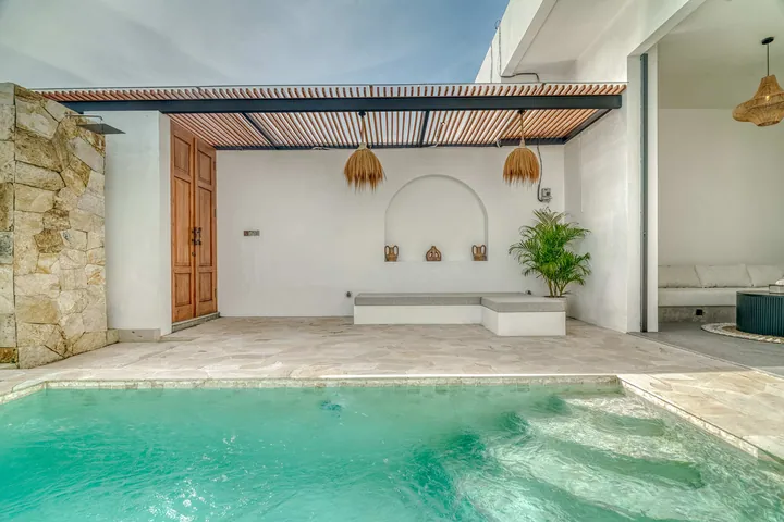 Courtyard pool with stepped entry facing a stone terrace, arched wall niche and timber pergola.