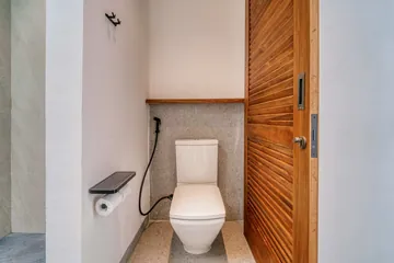 Toilet and handheld bidet beside a wood slatted door in a pale stone bathroom.