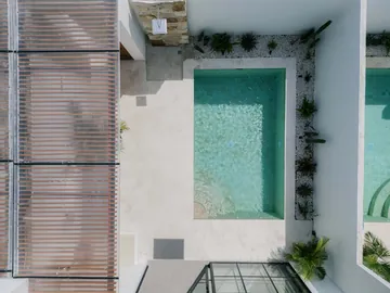 Overhead view of a narrow turquoise pool beside timber shade and pale paving.