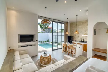 Bright open-plan room with sectional seating, kitchen island and courtyard visible through glass.