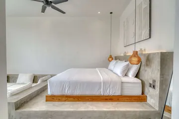 A white bed on a timber base, with pendant lamps and a ceiling fan.