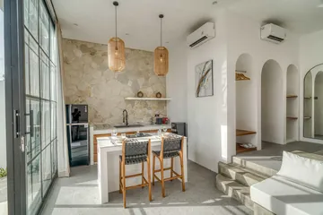 Kitchen island with dark chairs beside a stone wall and black-framed glass doors.