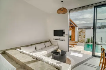 Sectional sofa and round coffee table facing a wall-mounted television, with glass doors to the pool.