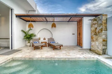 Stone courtyard with two cushioned loungers beneath a timber pergola and white arched wall.