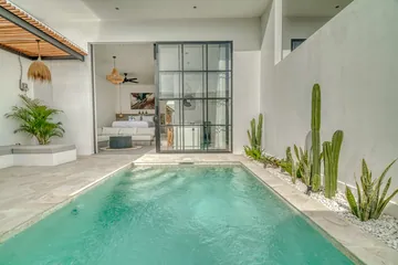 Turquoise courtyard pool bordered by stone paving, plants and a glass-walled room.