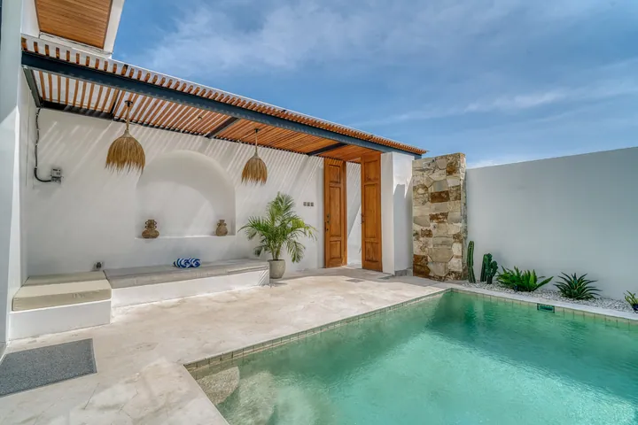 Courtyard pool framed by pale walls, timber roof slats and green planting.
