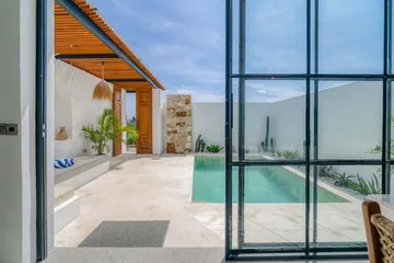 View through a glass doorway toward a pale pool terrace and white wall.