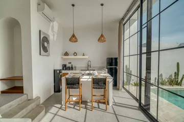 Dining island with four chairs and a kitchen shelf beside tall black-framed glazing.