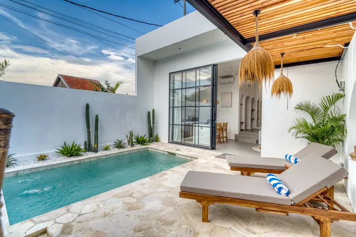 Turquoise courtyard pool, timber loungers and woven pendants beneath a slatted roof.