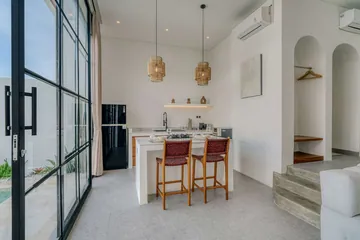 Kitchen counter and dining stools beside a glass wall and open-plan room.