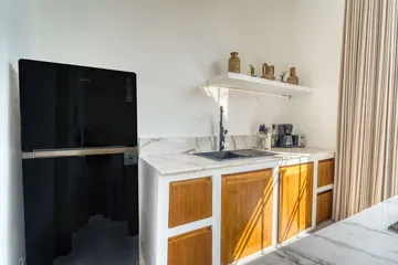 Compact kitchen with black refrigerator, countertop cooktop, white worktop and wood-front cabinets.