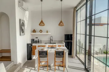 Kitchen with dark chairs and wood-front cabinetry, viewed beside the full-height glass wall.