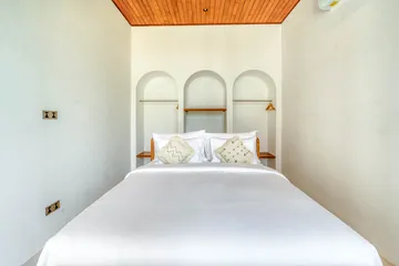 A white bed framed by three arched niches beneath a timber ceiling.
