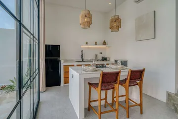 Kitchen counter with dark woven stools, a black refrigerator and tall glazing.