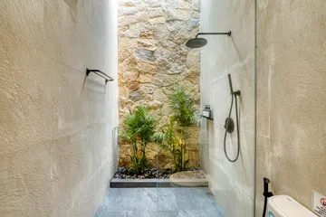 A shower beside a stone wall and a narrow planted recess.