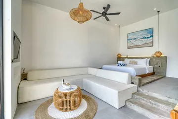 White sectional and round woven coffee table in front of a raised bed beneath pendant lights.