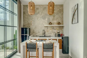 Stone-backed kitchen with a dining island and dark chairs beside black-framed glazing.