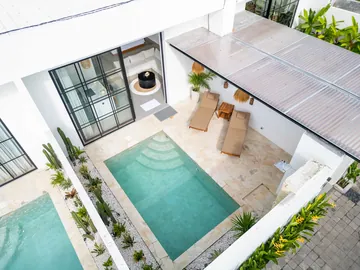 Aerial view into a courtyard pool with stepped entry, loungers and black-framed glazing.