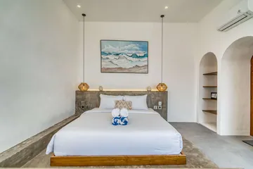 Low bed beneath framed coastal artwork, with arched niches and a ceiling fan.