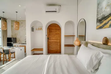 View from the bed toward an arched timber door, an arched mirror and the kitchen corner.